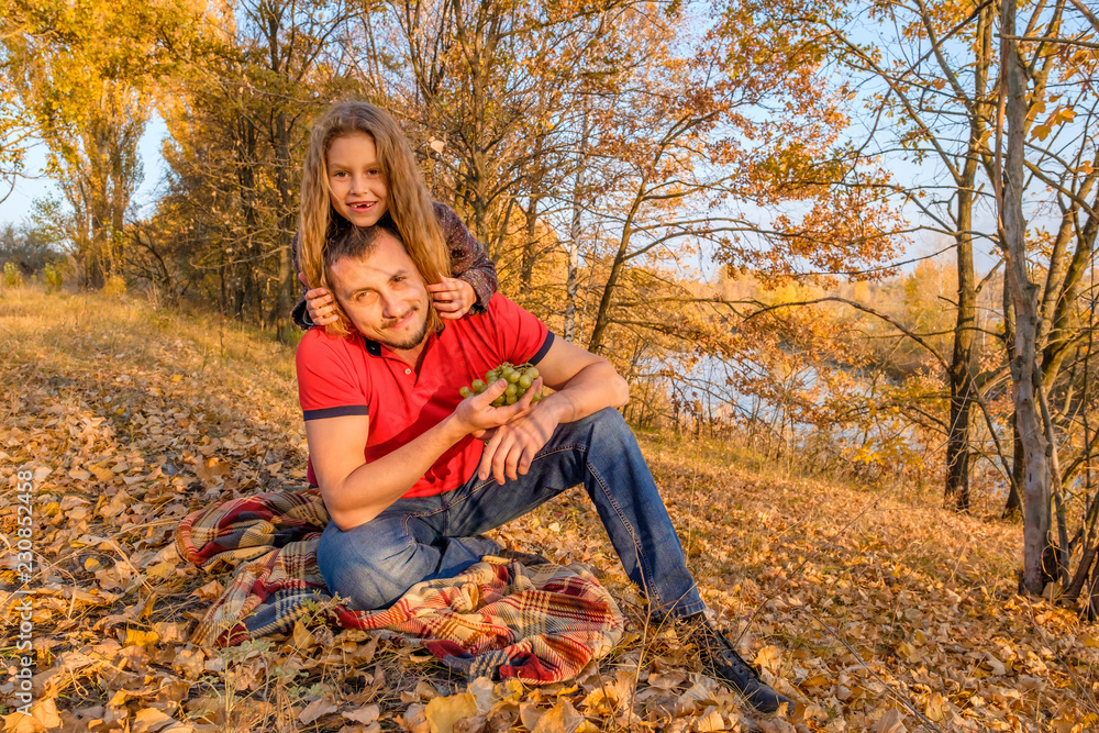 Young bearded father and his cute little daughter sitting on the fall leaves and having fun in the autumn park near the river. Concept of parenting and happy family. Young bearded father and his cute little daughter sitting on the fall leaves and having fun in the autumn park near the river. Concept of parenting and happy family.