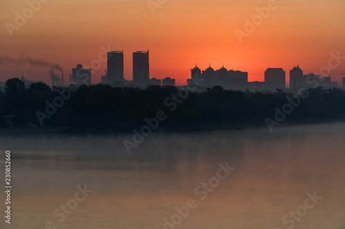 Silhouette of a city buildings on a horizont in a rays of red rising sun over Dneper, Kyiv, Ukraine photo