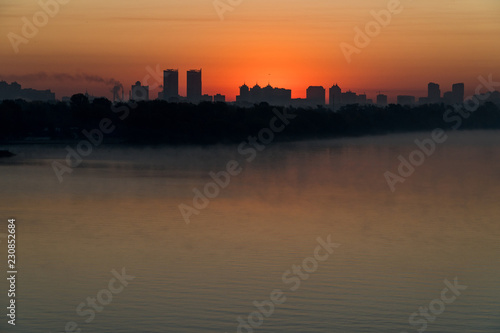 Silhouette of a city buildings on a horizont in a rays of red rising sun over Dneper  Kyiv  Ukraine