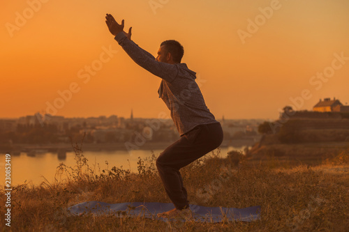 Man doing yoga on sunset with city view,Chair Pose /Utkatasana.