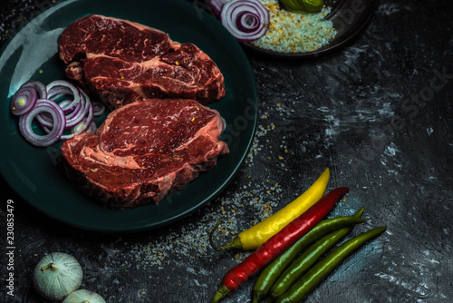 on a dark background fresh, red, raw beef and spilled coarse salt, next to it lies fresh vegetables