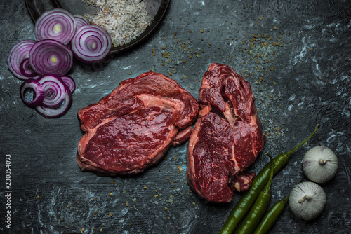 on a dark background fresh, red, raw beef and spilled coarse salt, next to it lies fresh vegetables