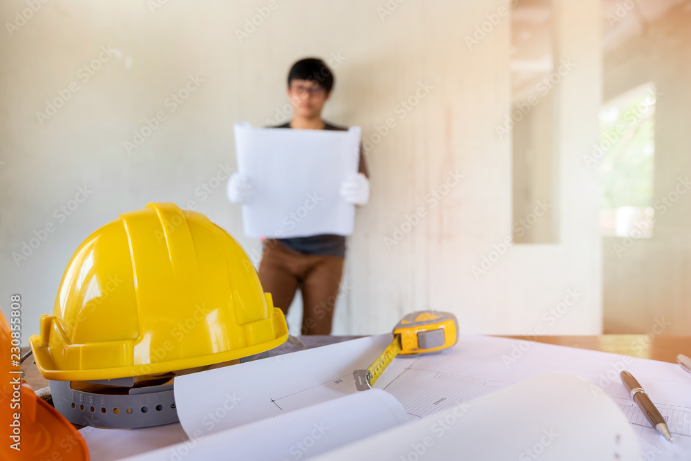 Helmet and blueprint on desk in front of Engineer or architect in construction site. Helmet and blueprint on desk in front of Engineer or architect in construction site.