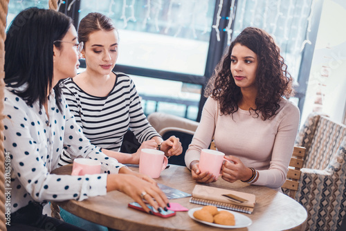 In the cafeteria. Beautiful nice women sitting together around the table while having tea