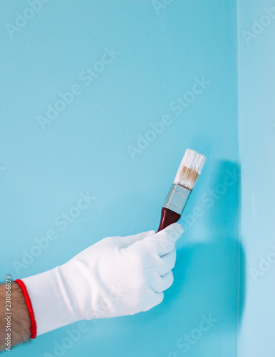 Image of man holding paintbrush in front of blue wall.