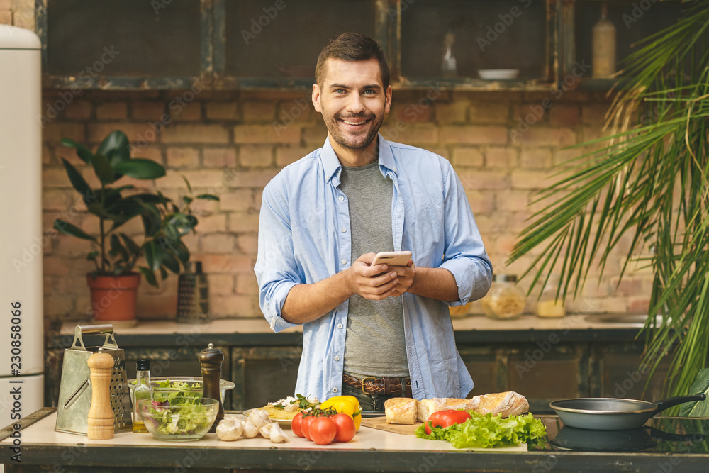 Man preparing delicious and healthy food in the home kitchen on a sunny day. Using phone for searching recipes. Man preparing delicious and healthy food in the home kitchen on a sunny day. Using phone for searching recipes.