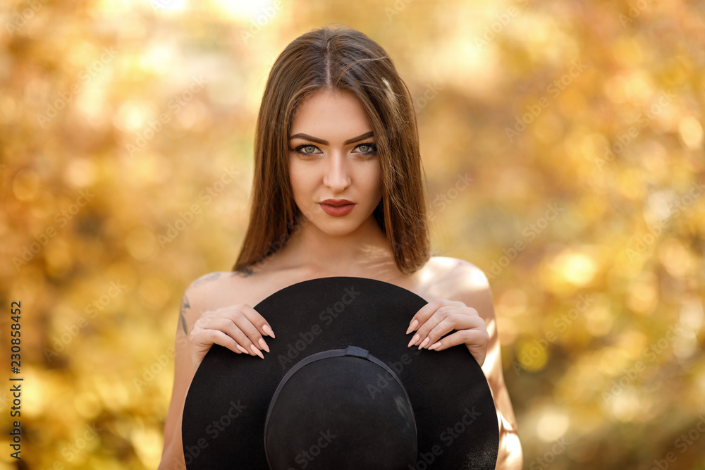Naklejka premium beautiful woman in black dress and hat in autumn