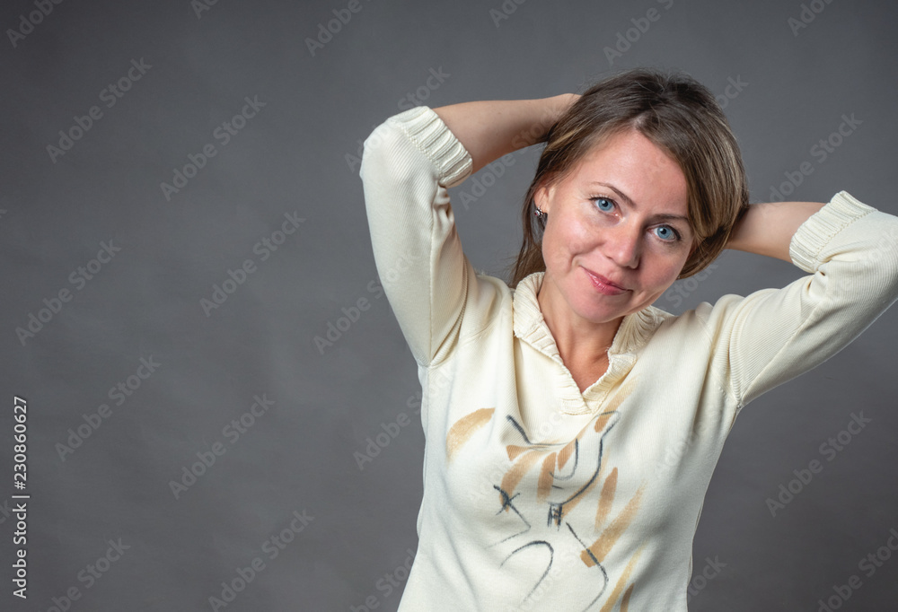 Naklejka premium Woman emotion. The young woman gathered her hair with her hands on the back of her head. Portrait of a smiling girl. Language of body. Portrait of woman over gray background shooting in studio