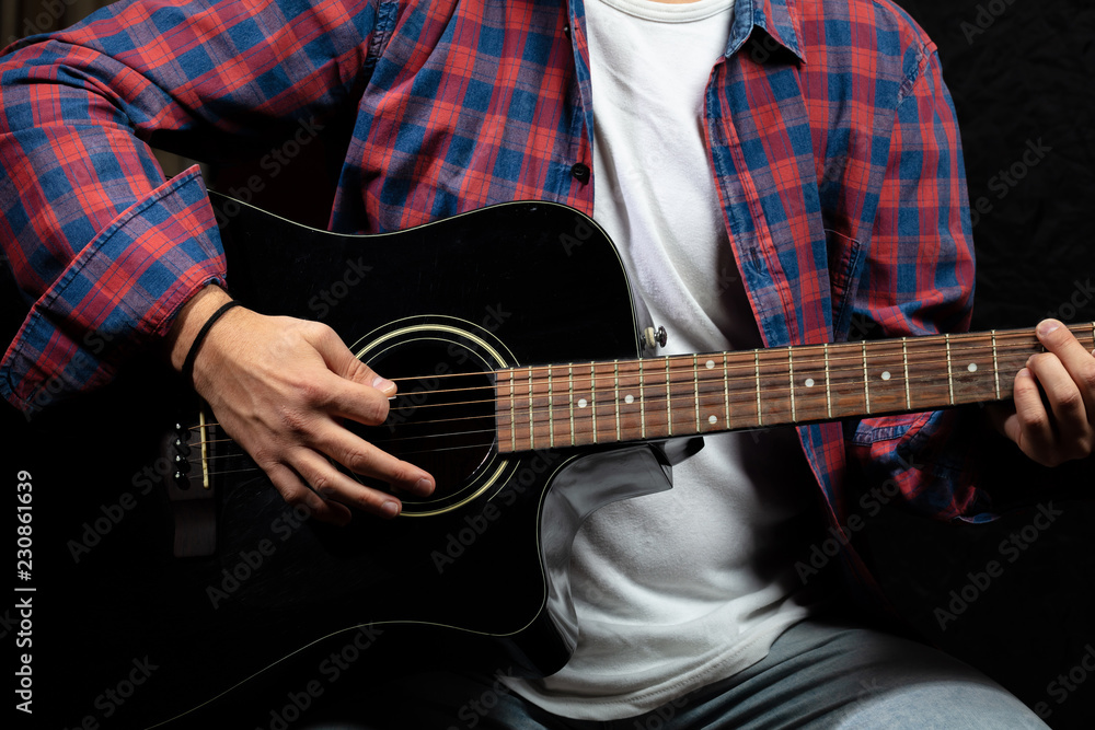 Fototapeta premium Young man playing guitar, close up view, dark background