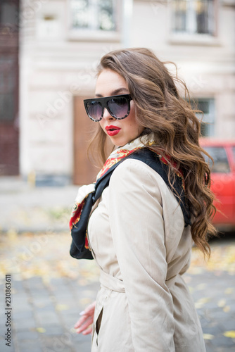 Young beautiful stylish woman walking down the street on a cold winter snowy day. Fashionable girl wearing black blouse and trousers and white fur coat. Female with long curly hair.