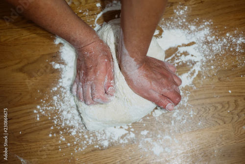 Hands kneading raw dough on wooden table