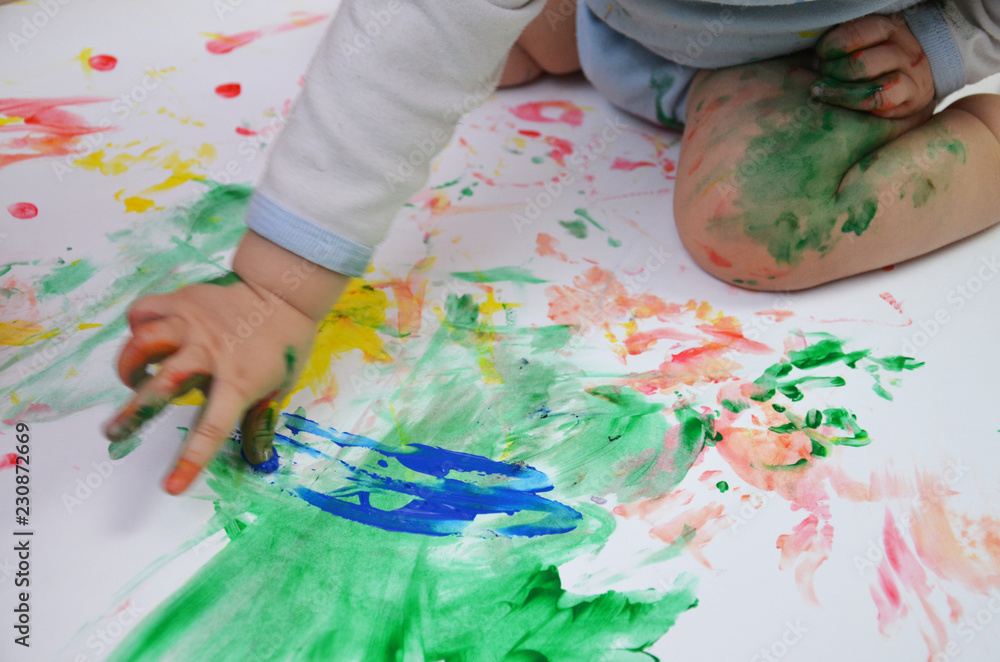 Painted colorful child hand against white background. girl draws her fingers multicolored paints on white paper. paint cans near Painted colorful child hand against white background. girl draws her fingers multicolored paints on white paper. paint cans near