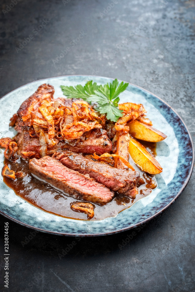 Traditioneller Zwiebelrostbraten aufgeschnitten mit Zwiebel und Bratkartoffel und Sauce als closeup auf einem Teller mit Textfreiraum Traditioneller Zwiebelrostbraten aufgeschnitten mit Zwiebel und Bratkartoffel und Sauce als closeup auf einem Teller mit Textfreiraum