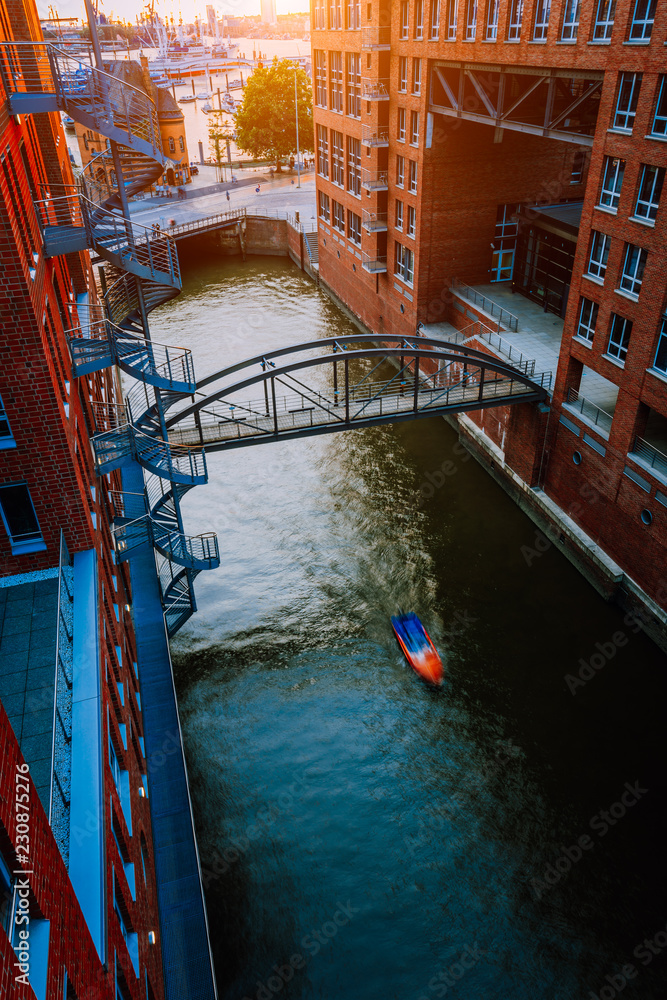 Small Boat under bridge over canal between red brick buildings in the old warehouse district Speicherstadt in Hamburg in golden hour sunset light, Germany. View from above
