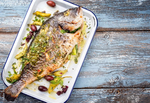 Fresh Greek barbecue gilthead seabream with peperoni and Kalamata olives as top view in a white skillet photo