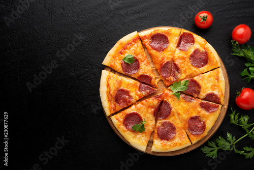 Pepperoni pizza, tomatoes and parsley. Tasty pepperoni pizza on black stone background. Overhead view of italian pizza.