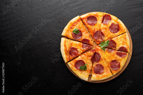 Pepperoni pizza, tomatoes and parsley. Tasty pepperoni pizza on black stone background. Overhead view of italian pizza.
