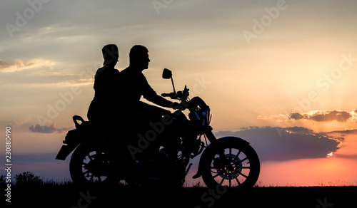 silhouette of a young couple man and woman on a motorcycle on sunset background
