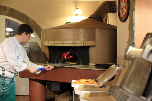Piekarz wyjmuje pizze z pieca opalanego drewnem.
