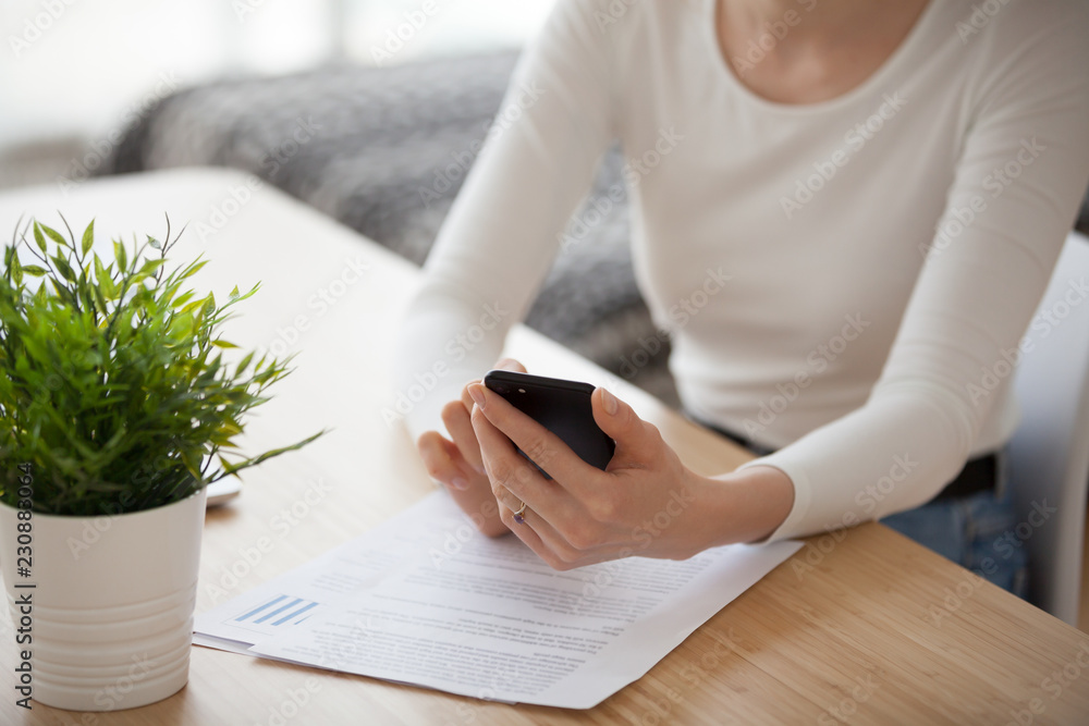 Φωτογραφία Close up millennial woman sitting at the desk at home holding mobile phone typing chatting messaging e-mail or reading news in internet