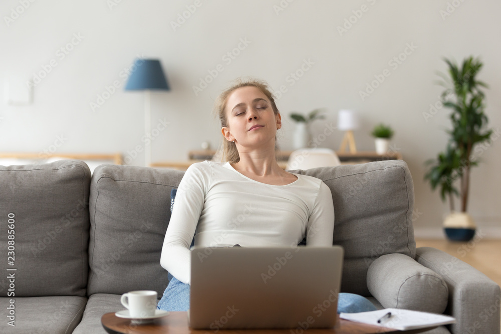 Attractive young tired millennial student woman sitting on couch in living room at home opposite of computer sleeping. Overworked fatigued serene female nap after studying. Hard working day concept