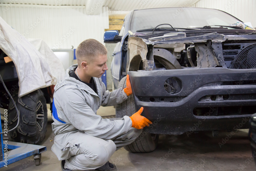 Repair and painting car car mechanic. Auto mechanic worker painting car in a paint chamber during repair work. Auto repairman plastering autobody bonnet. 