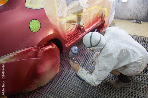 Repair and painting car car mechanic. Auto mechanic worker painting car in a paint chamber during repair work. Auto repairman plastering autobody bonnet.  photo