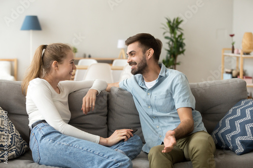 Affectionate cheerful married couple in love or friends spend free time together on weekend talking laughing communicating sitting in living room at home. Dating and not boring with each other concept