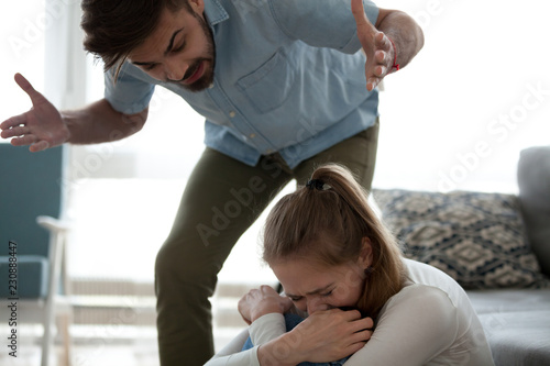 Unhappy crying frightened woman and aggressive man quarrelling at home. Angry husband emotionally arguing screaming shouting to scared wife psychological emotional abuse and domestic violence concept
