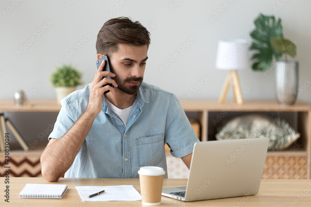 Serious businessman sitting at the desk typing chatting using computer and talking by cellphone. Confident employee hard working busy during work day solving business matters agent talking with client Serious businessman sitting at the desk typing chatting using computer and talking by cellphone. Confident employee hard working busy during work day solving business matters agent talking with client