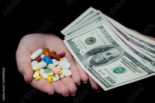 Money and pills in hands, isolated on black. Wasting too much money on medication. Drug addiction concept