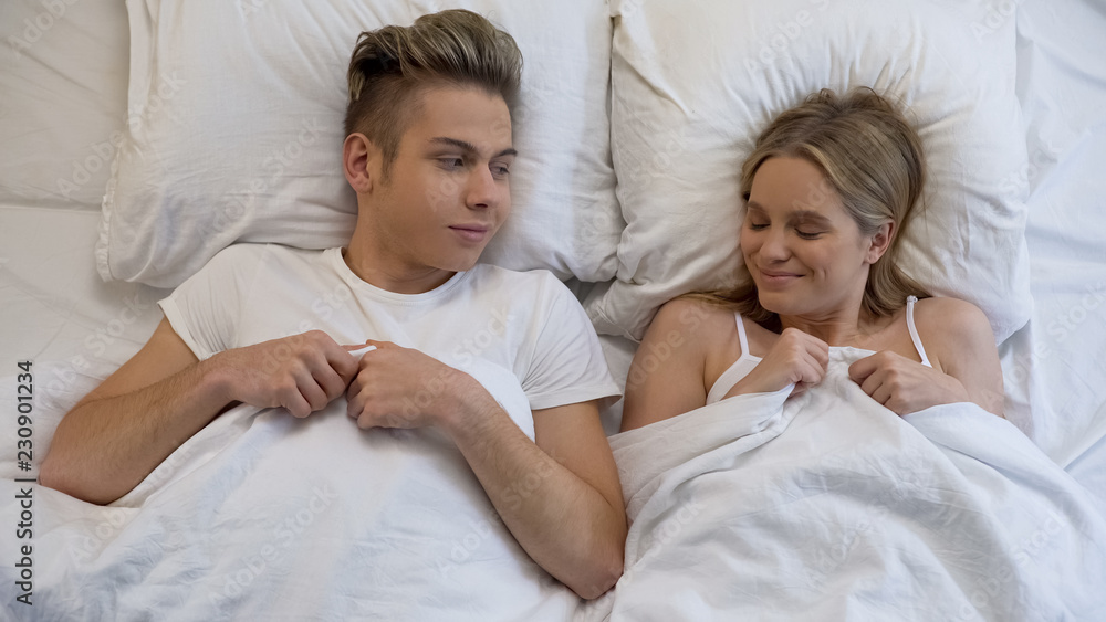 Happy couple smiling to each other lying in bed, first intimacy, love experience Happy couple smiling to each other lying in bed, first intimacy, love experience