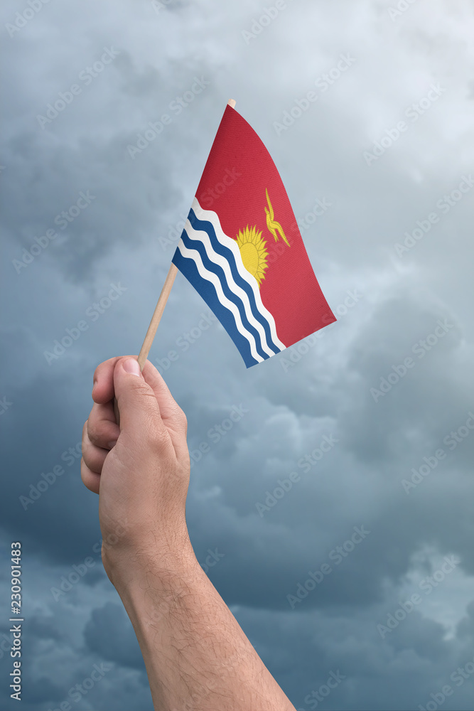 Hand holding Kiribati flag high in the air, with a stormy, cloudy sky