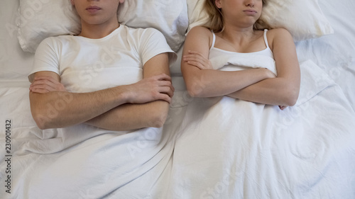 Couple lying in bed after quarrel, looking at each other angrily, conflict