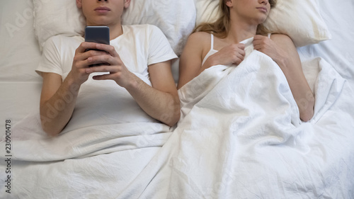 Boyfriend playing smartphone games in bed, ignoring girlfriend, couple problem