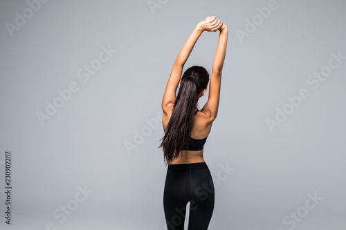 Back view portrait of a young woman stretching hands isolated on a gray background