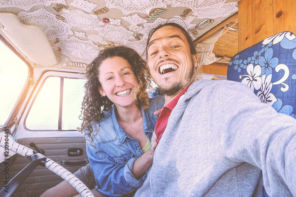Happy couple taking a selfie inside a vintage minivan - Travel people excited and ready for driving to road trip with a van camper - Vacation, love, relationship lifestyle concept