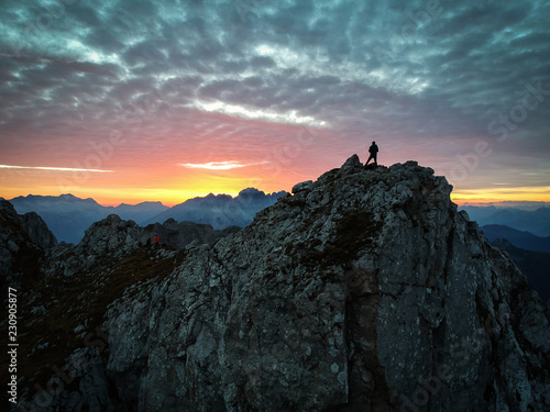 Silhouette of man enjoying sunset in top of the mountains with colorful clouds in background