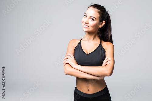 Portrait of a beautiful fitness woman with crossed arms on grey background