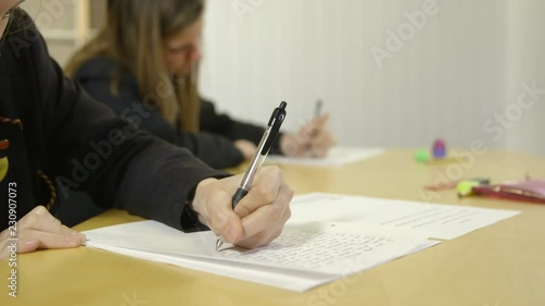 Tracking shot of two girls in school uniform writing in an exam in a school or college. photo