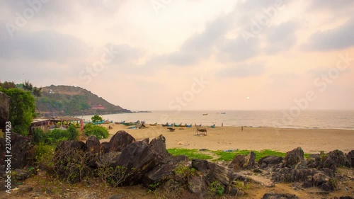 Tourists walking at sunset with moving clouds behind Rama Temple and rocky outcropping on the main beach at South Indian holy village of Gokarna, Karnataka, India. Stationary time-lapse footage photo