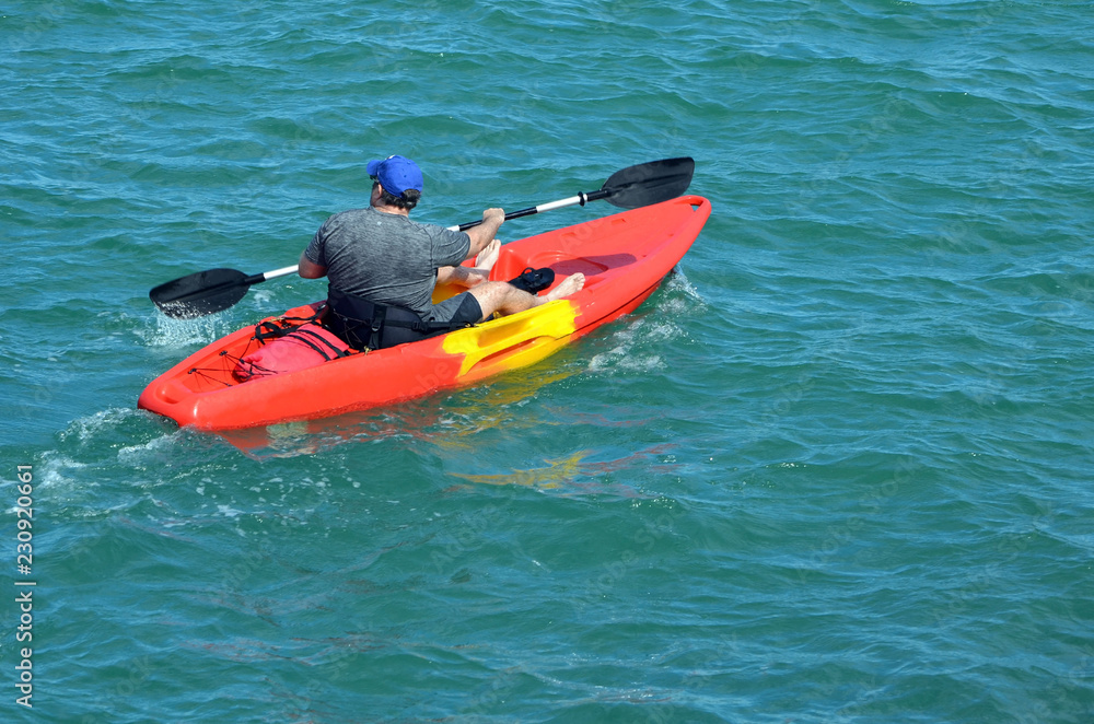 Kayaker paddling a bright orange single place kayak on the Florida Intra-Coastal Waterway.
