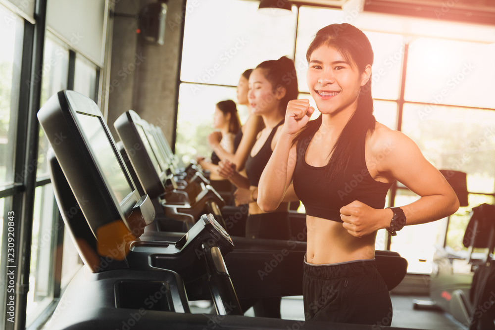 Happy woman with group of young people running or jogging on treadmills in modern sport gym. exercise and sport concept. Happy woman with group of young people running or jogging on treadmills in modern sport gym. exercise and sport concept.