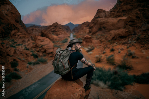 Man wearing hat sitting on rock during sunset