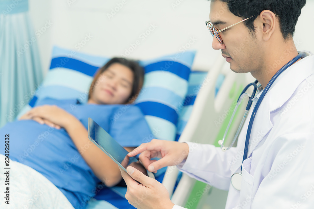 Obraz premium Asian young pregnant woman lying down talking and visit to her doctor man in a room.