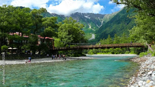 Tourists enjoying daytime around beautiful Kappa Bridge and turquoise Azusa river in sunny Kamikochi, surrounded by moving clouds near Mount Hotaka, Okuhotaka. 30fps RL pan motion timelapse footage photo