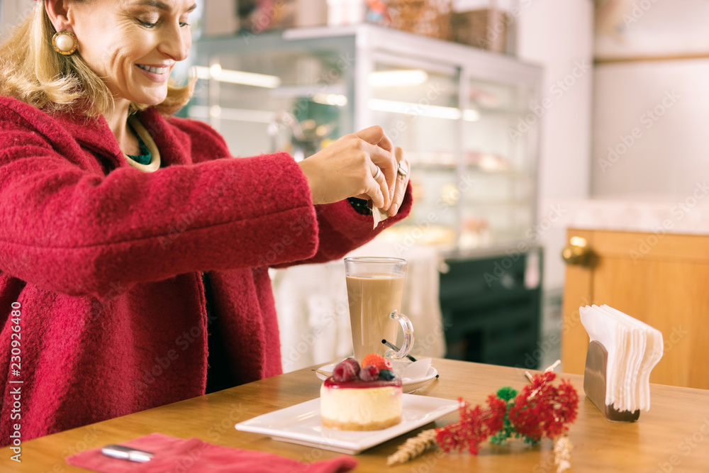 Smiling woman. Smiling mature fashionable woman with facial wrinkles putting sugar in her coffee