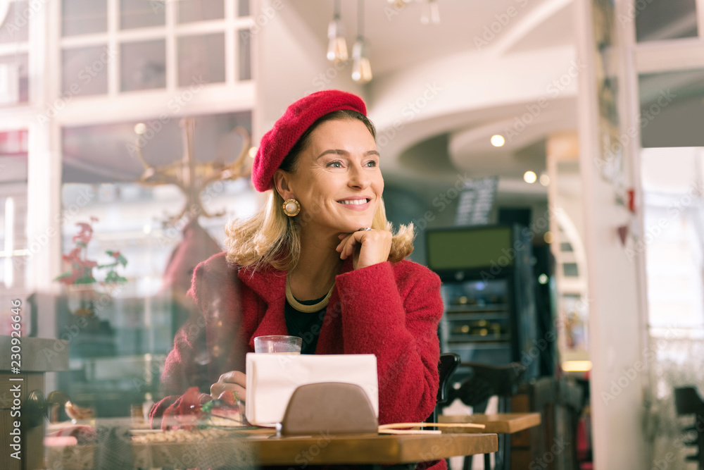 Look into window. Elegant appealing mature woman feeling amazing sitting in bakery and looking into window