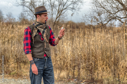 Old fashioned retro steampunk man in hat, wool vest, scarf with pocket watch in hand and smoking pipe in mouth. HDR image