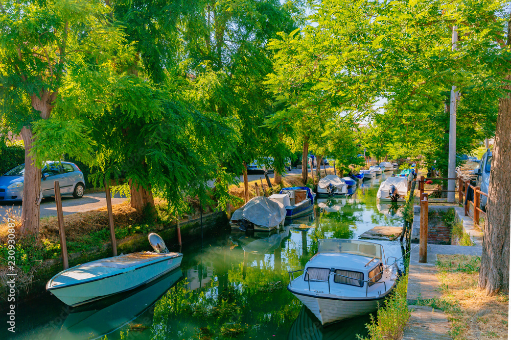 Canal and boats under trees in Lido of Venice, Italy